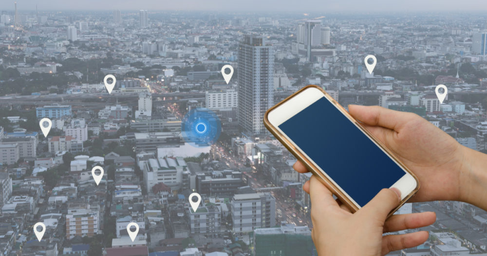 La main d'une femme utilisant un smartphone mobile recherche l'emplacement sur la carte et l'épinglette au-dessus du paysage urbain en bleu